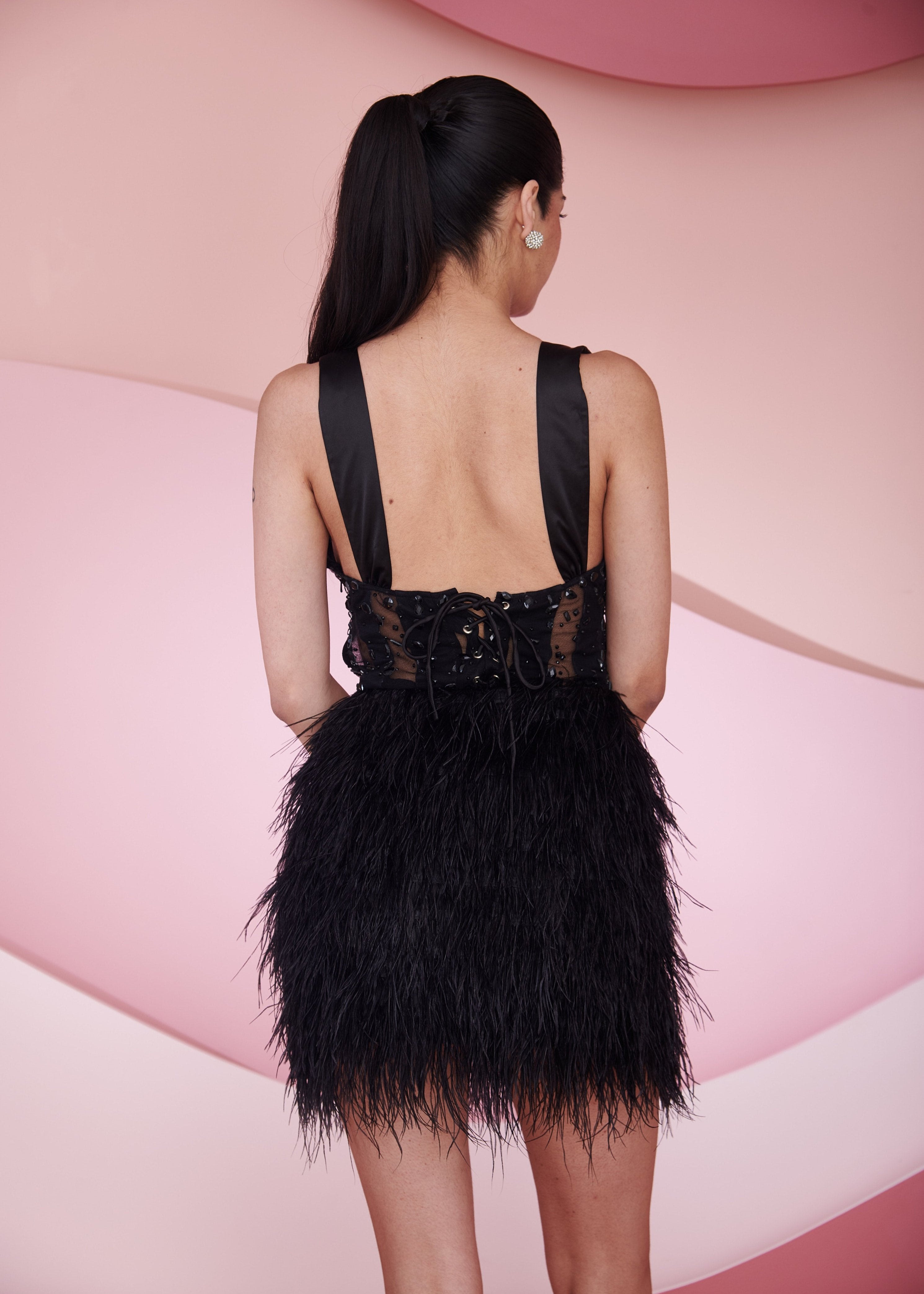 Chic woman in an Airi Black Embroidered Rhinestone and Feather Corset Mini Dress looking glamorous