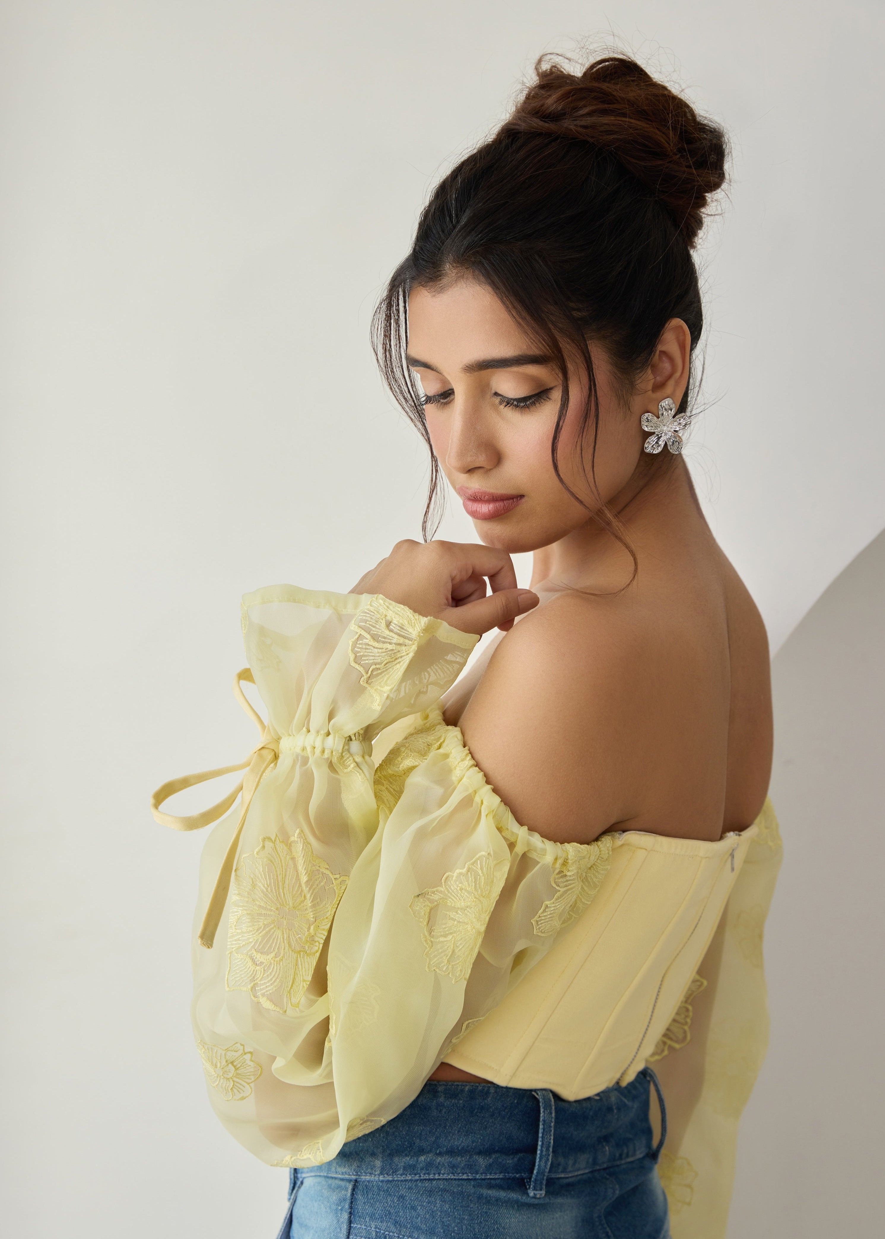 A yellow corset top with embroidered details and organza sleeves.