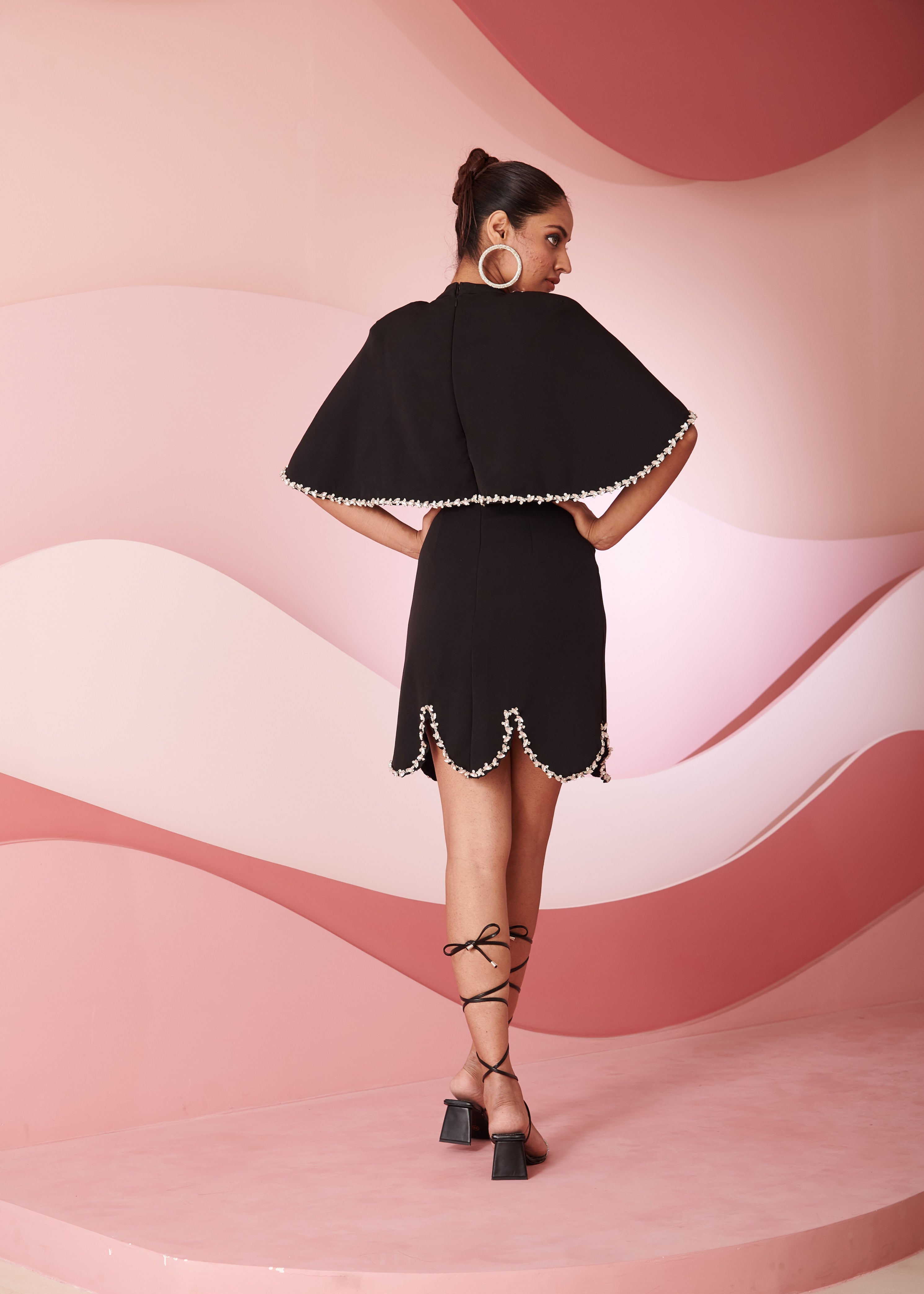 Chic woman in a Yuka Black Rhinestone Cape Mini Dress radiating glamour and style